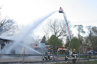 firemen and a crane spraying water on a burning building
